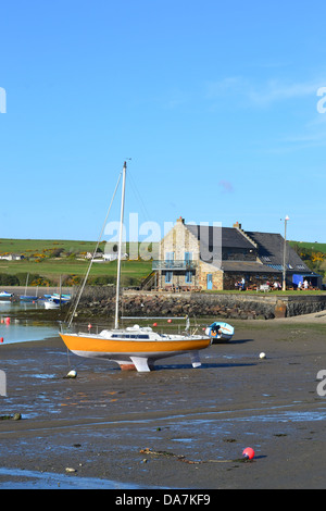 Gelbe Segelboot mit abgesenkten Segel ruht auf dem Sand bei Ebbe, unter blauem Himmel. Stockfoto