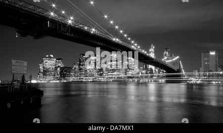 Brooklyn Bridge und die Skyline der Innenstadt Manhattan in der Dämmerung mit Lichtspuren von einem vorbeifahrenden Boot Stockfoto