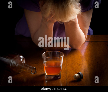 Konzept-Foto für Alkoholismus Krankheit zeigt Whiskeyglas und leere Flasche mit Frau übergibt Gesicht deprimiert über das Glas Stockfoto