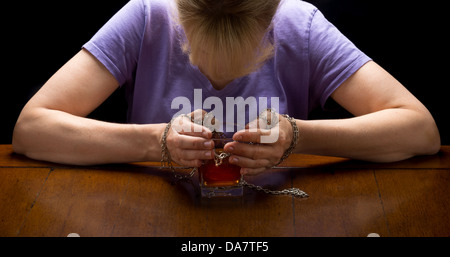 Konzept Foto Nahaufnahme für Alkoholismus Krankheit zeigt Hände angekettet an Whiskeyglas mit Frauenkopf schwebt. Stockfoto