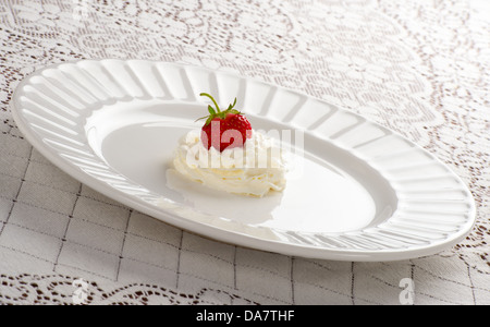 Erdbeere sitzt im Strudel der süßen Sahne auf weißen Teller Stockfoto