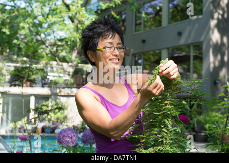 Eine asiatische Frau arbeitet in ihrem schönen Garten mit Haus im Hintergrund Stockfoto