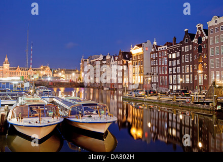 Stadt Amsterdam in den Niederlanden in der Nacht, historischen Wohnhäusern mit Reflexionen über Wasser und Boote für Kanal-Touren bereit. Stockfoto