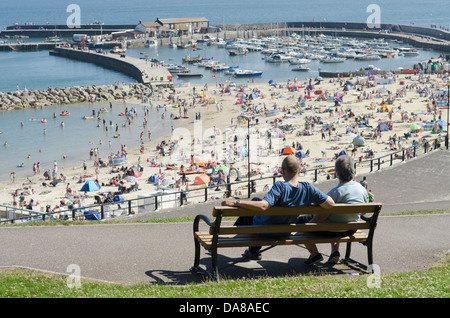 Zwei Menschen sitzen auf einer Bank anzeigen The Cob Lyme Regis Harbour von Lister Gärten Stockfoto