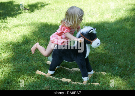 Kind blonde Mädchen auf einem Schaukelpferd außerhalb, Sommergarten Stockfoto