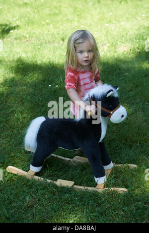 Kind blonde Mädchen auf einem Schaukelpferd außerhalb, Sommergarten Stockfoto