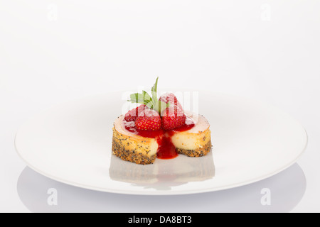 Käsekuchen mit Erdbeeren, roten Coulis und Minze auf weißen Teller. Stockfoto
