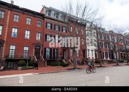 Frau reitet ein Capital Bikeshare Fahrrad vor alten historischen Backstein-Stadthäusern auf Jackson findet in Washington D.C. Stockfoto