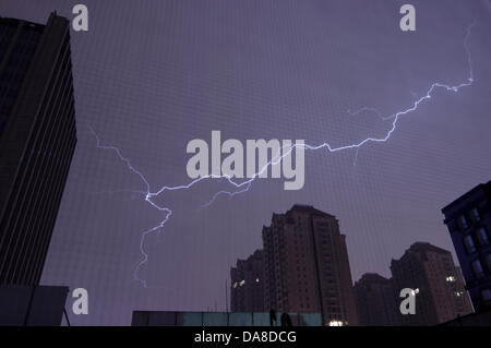 Blitze durchziehen den Himmel während eines Gewitters in der Nacht, gesehen über den beleuchteten Fenstern eines Wohnhauses im Chaoyang Bezirk von Peking, China. © Olli Geibel Stockfoto