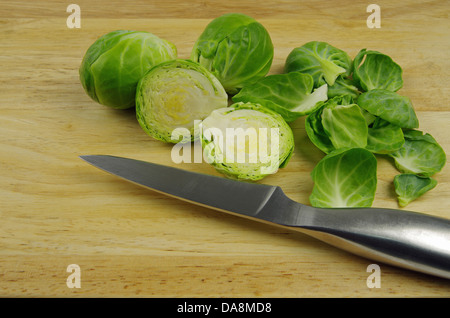 Rosenkohl geschnitten und geschält auf ein hölzernes Brett und Silber Wiegemesser Stockfoto