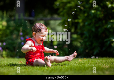 Ein Baby quietscht vor Freude, wie sie mit Wasser aus dem Schlauch kühlt. Stockfoto