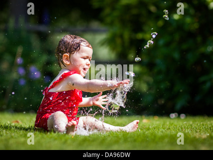 Ein Baby quietscht vor Freude, wie sie mit Wasser aus dem Schlauch kühlt. Stockfoto