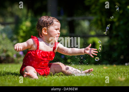 Ein Baby quietscht vor Freude, wie sie mit Wasser aus dem Schlauch kühlt. Stockfoto