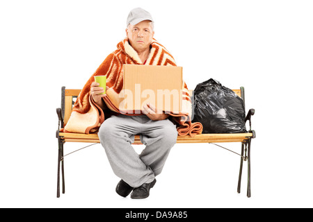 Obdachlose reifer Mann sitzen auf einer Bank, seine Habseligkeiten neben ihm hält einen leeren Karton Stockfoto