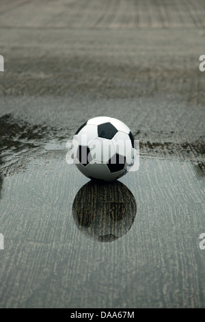 Es ist ein Foto von einem Fußball-Ball, der auf eine nasse Spielplatz in einer Wasserpfütze steht Stockfoto