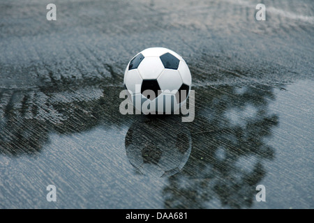 Es ist ein Foto von einem Fußball-Ball, der auf eine nasse Spielplatz in einer Wasserpfütze steht Stockfoto