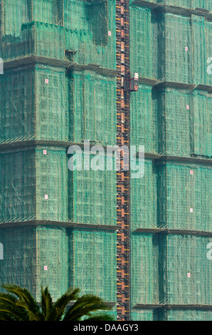 Bambus-Gerüst und grüne Netting umgibt eine Neuentwicklung Wohneigentum auf dieser Baustelle Taipa. Stockfoto