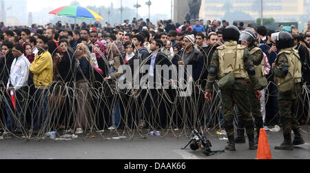 Demonstranten versammeln sich hinter eine Lücke im Stacheldraht Barrikade in einer Straße, wie ägyptische Soldaten sie zu überprüfen, bevor sie dem Tahrir-Platz in Kairo, Ägypten, am 5. Februar 2011 treten. Proteste gegen die Regierung trat ihre 12. Tag in Ägypten, als Lösungen Glühwein wird, wurden um eine Machtverschiebung herbeizuführen, um politischen Lähmung des Landes zu beenden.  Foto: Hannibal dpa Stockfoto