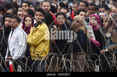 Demonstranten versammeln sich hinter eine Lücke im Stacheldraht Barrikade in einer Straße, wie ägyptische Soldaten sie zu überprüfen, bevor sie dem Tahrir-Platz in Kairo, Ägypten, am 5. Februar 2011 treten. Proteste gegen die Regierung trat ihre 12. Tag in Ägypten, als Lösungen Glühwein wird, wurden um eine Machtverschiebung herbeizuführen, um politischen Lähmung des Landes zu beenden. .  Foto: Hannibal dpa Stockfoto