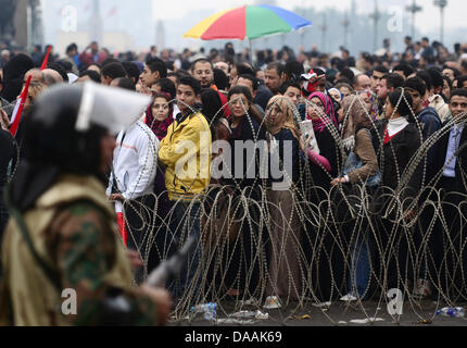 Demonstranten versammeln sich hinter eine Lücke im Stacheldraht Barrikade in einer Straße, wie ägyptische Soldaten sie zu überprüfen, bevor sie dem Tahrir-Platz in Kairo, Ägypten, am 5. Februar 2011 treten. Proteste gegen die Regierung trat ihre 12. Tag in Ägypten, als Lösungen Glühwein wird, wurden um eine Machtverschiebung herbeizuführen, um politischen Lähmung des Landes zu beenden. .  Foto: Hannibal dpa Stockfoto