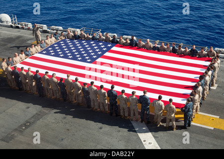Matrosen und Marinesoldaten Anzeigen der nationalen Flagge zu Ehren des Independence Day auf amphibischer Angriff Schiff USS Kearsarge (LHD-3). Kearsarge ist das Flaggschiff für die Kearsarge amphibische bereit Gruppe und mit der eingeschifften 26. Marine Expeditionary Unit Stockfoto