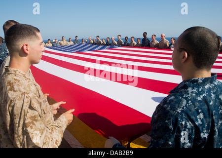 Matrosen und Marinesoldaten Anzeigen der nationalen Flagge zu Ehren des Independence Day auf amphibischer Angriff Schiff USS Kearsarge (LHD-3). Kearsarge ist das Flaggschiff für die Kearsarge amphibische bereit Gruppe und mit der eingeschifften 26. Marine Expeditionary Unit Stockfoto