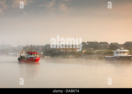 Ein kleines Fischerboot verlässt Walberswick Hafen, da die Sonne aus den frühen Morgennebel brennt. Stockfoto