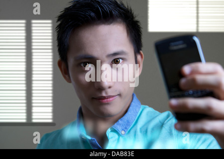 Ein junger Mann, ein Foto auf seinem Handy in einem Spiegel. Tragen von farbigen Kontaktlinsen, England Stockfoto