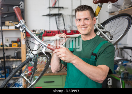 Zweiradmechaniker tragen eine Fahrrad in Werkstatt lächelnd in die Kamera Stockfoto