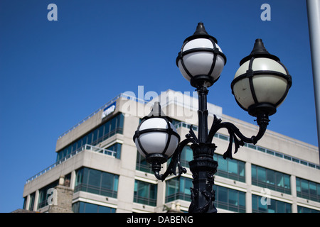 Eine kunstvolle Straßenlaterne mit drei Globen steht vor einem modernen Bürogebäude und blauem Himmel in Dublin, Irland, im Jahr 2013. Stockfoto