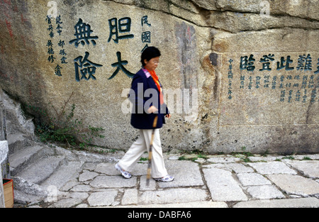 Chinesische Frau, die mit einem Stock auf dem Berg Hua Shan in der Nähe der Stadt Huayin in der chinesischen Provinz Shaanxi läuft. Der Berg Hua ist der westliche Berg der fünf Großen Berge Chinas und hat eine lange Geschichte von religiöser Bedeutung. Stockfoto