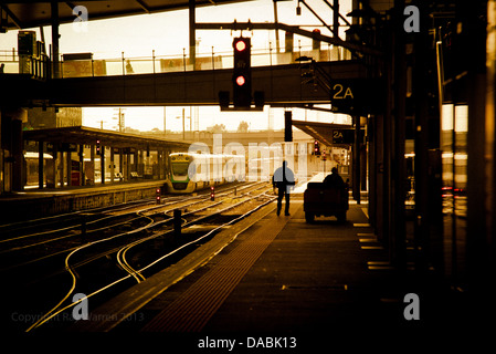 Eine Person ist im Gegenlicht Silhouette, wie er auf einer leeren Plattform in einem höhlenartigen Bahnhof auf einen Zug wartet. Stockfoto