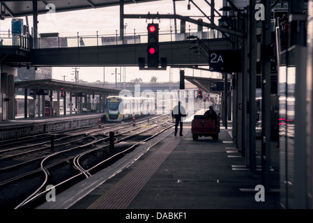 Eine Person ist im Gegenlicht Silhouette, wie er auf einer leeren Plattform in einem höhlenartigen Bahnhof auf einen Zug wartet. Stockfoto