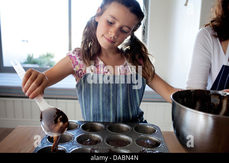 Junges Mädchen und ihre Mutter Gießen Sie Kuchenteig in eine Backform Tablett in einer Küche - Stonehurst Estate, Kapstadt, Südafrika. Stockfoto