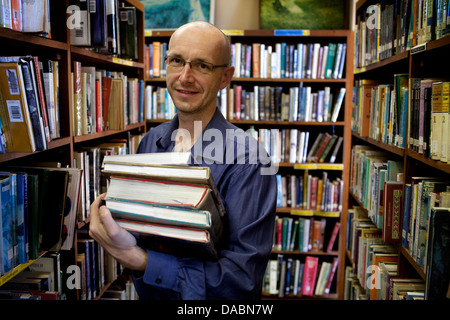 Cape Town, Südafrika. Michael hält Bücher in einer Bibliothek. Er ist umgeben von Regalen Bücher. 25. Februar 2013. Stockfoto