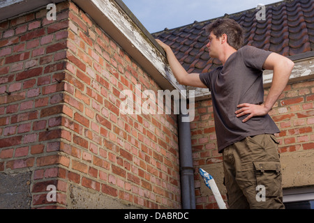 Junger Mann, das Dach eines alten Hauses stehen auf einer Leiter Inspektion Stockfoto