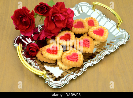 Herzförmige Kekse und Rosen sind auf einem Metalltablett Stockfoto