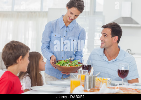 Hübsche Frau bringt einen Salat zu ihrer Familie Stockfoto