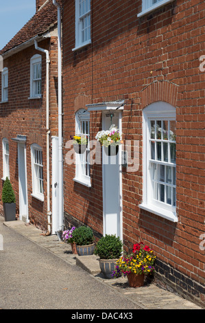 Blumenampeln und anderen Pflanzen zieren die Vorderseite der Reihenhäuser in Kersey, Suffolk, England. Stockfoto