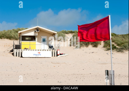 Eine rote Flagge vor Bohnenstroh Rettungsschwimmer am Strand Konstantin Bay Cornwall UK Stockfoto