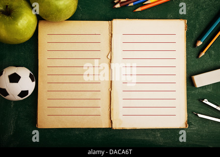 Aufgeschlagene Buch und die Schule-Versorgungsmaterialien, Tafel im Hintergrund. Stockfoto