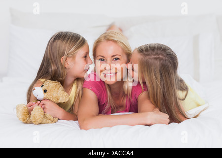 Zwillinge, die ihre Mutter im Bett küssen Stockfoto
