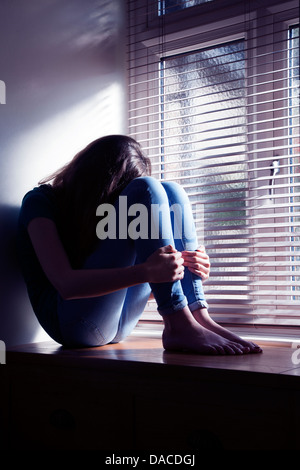 Teenager-Mädchen, Kopf neigte, sitzen an einem Fenster mit Licht herein. Stockfoto