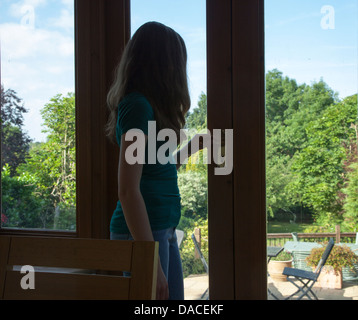 Ein junges Mädchen, Blick durch eine Glastür in einen Garten. Hinten/Seitenansicht. Stockfoto