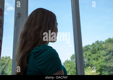Ein junges Mädchen, Blick aus dem Fenster. Hinten/Seitenansicht. Stockfoto