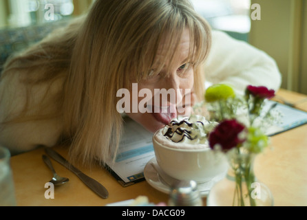 Frau lecken Schlagsahne vom oberen Rand einer Tasse. Stockfoto
