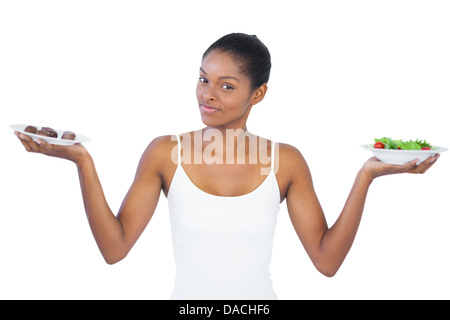 Hübsche Frau, die Entscheidung zu essen gesund oder nicht Stockfoto