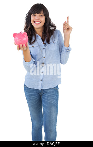 Lächelnde junge Frau mit Sparschwein mit ihrem finger Stockfoto