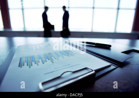Nahaufnahme von einem Finanzbericht mit den Silhouetten von Geschäftsleuten im Hintergrund Stockfoto