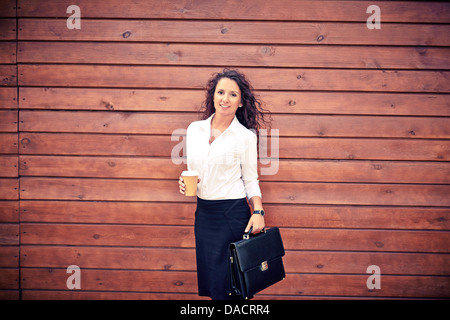 Bild der jungen Unternehmerin mit Kaffee und Aktenkoffer Blick in die Kamera Stockfoto